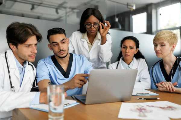 Equipo multiétnico concentrado de médicos sentados en la mesa, utilizando un ordenador portátil —  Fotos de Stock