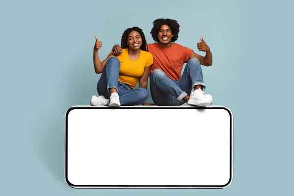 Couple noir positif assis sur grand smartphone avec écran blanc — Photo