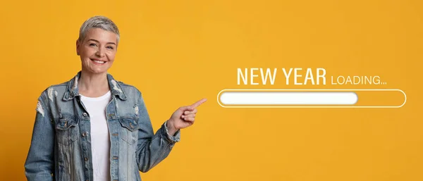 Leende mogen kvinna pekar finger åt sidan på nyår lastning process bar på orange studio bakgrund, collage — Stockfoto