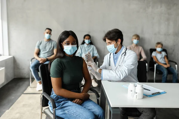 Egy fiatal fekete hölgy arcmaszkban, akit beoltottak a klinikán. — Stock Fotó