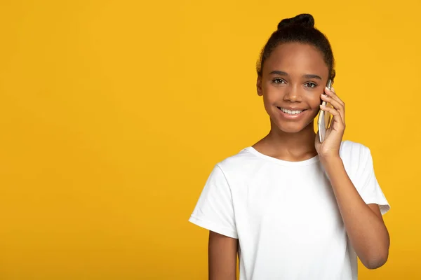 Smiling adolescent pretty african american female pupil in white t-shirt calls and talks with parents on phone — Stock Photo, Image