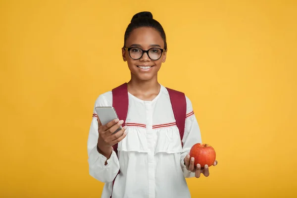 ハッピースマート若いですアフリカ系アメリカ人の女の子学生で眼鏡でバックパックホールドスマートフォンと赤リンゴ — ストック写真