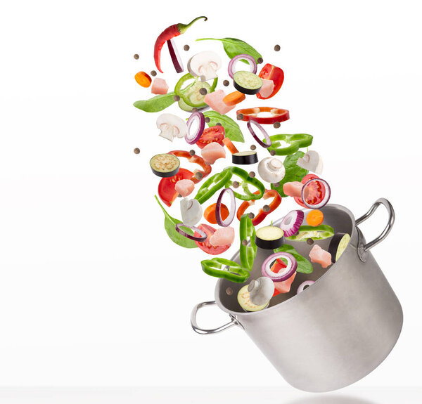 Fresh vegetables and raw meat flying into steel stewpot