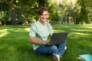 Uzaktan eğitim konsepti. Bilgisayarı ve kitapları olan mutlu bir öğrenci parktaki çevrimiçi derslere katılıyor. Dışarıdaki web konferansına katılan heyecanlı adam.