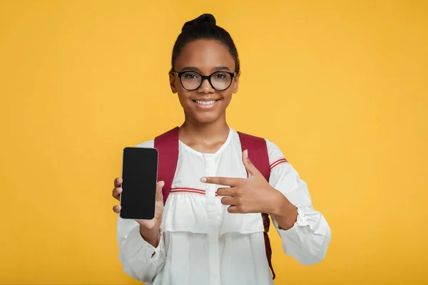 Soddisfatto intelligente adolescente nero pupilla in occhiali con zaino mostra dito a smartphone con schermo bianco — Foto Stock