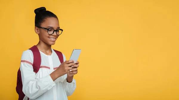 Allegro intelligente giovane afro-americana alunni signora in occhiali con zaino digitando messaggio su smartphone — Foto Stock