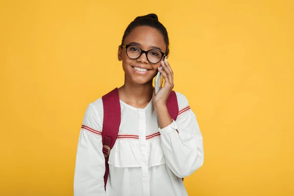 陽気なスマートティーンアフロアメリカの女の子学生で眼鏡でバックパックコールオン電話 — ストック写真