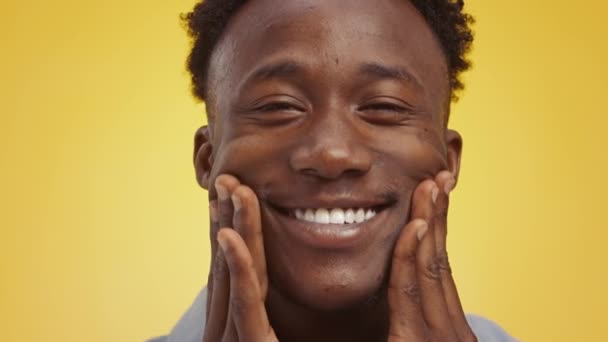 Verdadera felicidad. Primer plano retrato de un chico afroamericano sonriente y ancho masajeando sus mejillas con la cara sonriente — Vídeo de stock