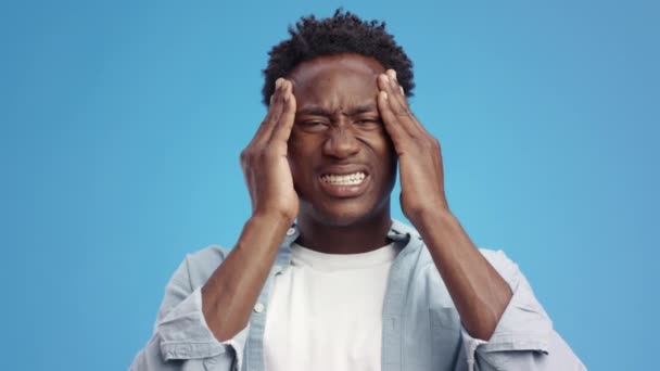 Ужасная мигрень. Молодой эмоциональный африканский американец массирует виски, страдает от острой головной боли. — стоковое видео