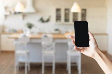 Yemek odasında akıllı ev uygulaması ya da iç tasarım web sitesi için cep telefonuyla tanınmayan bir kadın.