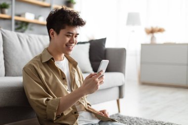 Evde akıllı telefon kullanan gülümseyen Asyalı adamın yakın çekimi.