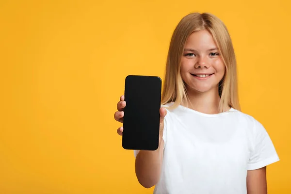 Usmívající se dospívající blondýnka studentská show telefon s prázdnou obrazovkou, izolované na žlutém pozadí — Stock fotografie