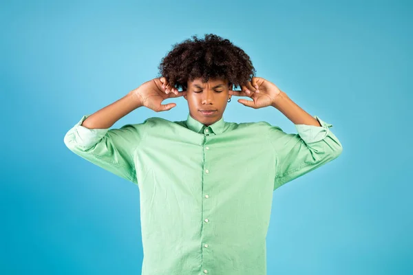 Afro-americano perturbado fechando os ouvidos com os dedos, protegendo do barulho alto sobre o fundo do estúdio azul — Fotografia de Stock