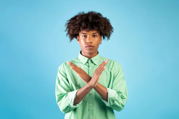 Sérieux noir adolescent guy montrant arrêter ou aucun geste, croiser les mains, détester ou nier quelque chose, fond bleu — Photo