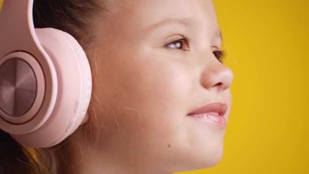 Музыка для детей. Закройте портрет милой улыбающейся маленькой девочки в розовых наушниках, открывающей глаза и смотрящей в сторону — стоковое видео