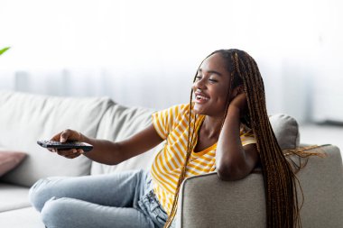 Rahat Afro-Amerikan genç kadın evde televizyon izliyor.