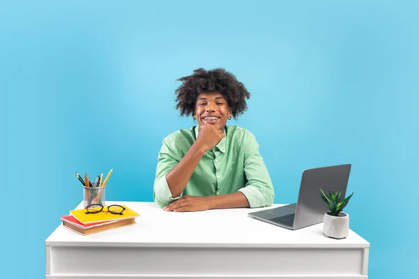 Koncepcja edukacji internetowej. Szczęśliwy Afroamerykanin w okularach siedzi przy biurku i używa laptopa, niebieskie tło — Zdjęcie stockowe