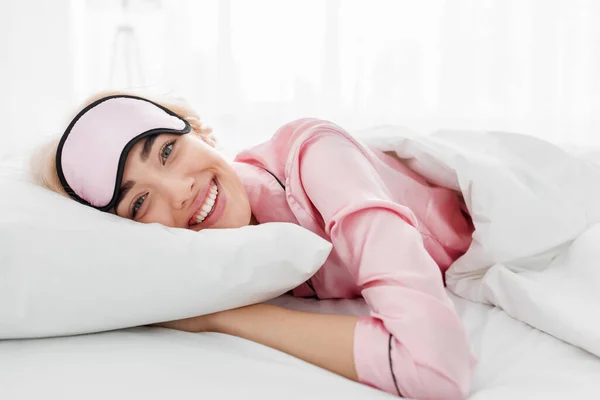 Sorrindo muito jovem mulher loira caucasiana em pijama rosa e máscara de sono desfrutando de bom dia — Fotografia de Stock