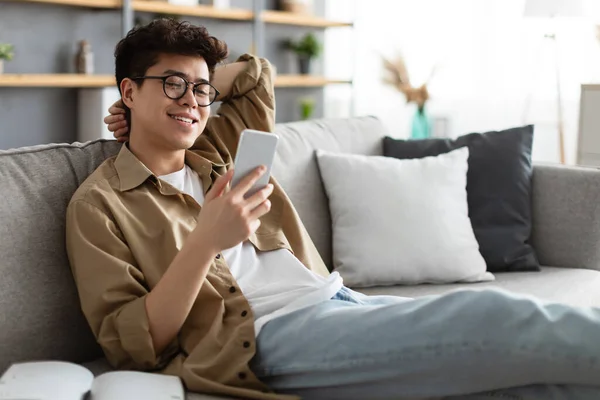 Smiling asian man in glasses using smartphone at home — Stock Photo, Image