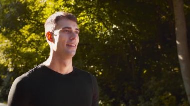 Genç adam parkta duruyor ve derin nefes alıyor güneşli bir sabahta kentsel olmayan bölgenin temiz havasının tadını çıkarıyor.