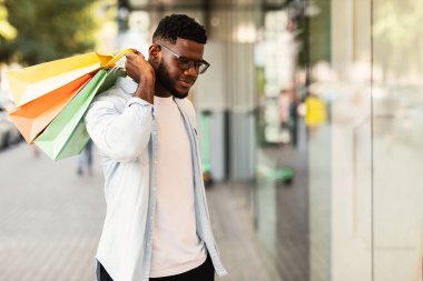 Alışveriş çantalı zenci adam alışveriş merkezinin camına bakıyor.