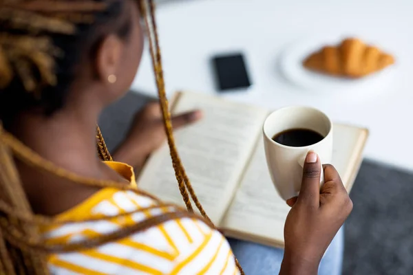 Mujer negra bebiendo café y leyendo libro en casa — Foto de Stock