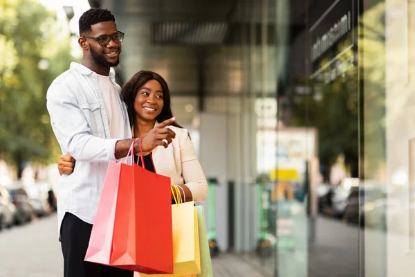 Retrato de casal negro com sacos de compras apontando para a janela — Fotografia de Stock