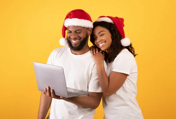 Säsongsförsäljning. Glad afrikansk amerikansk par tittar på bärbar dator och ler, står på gul bakgrund — Stockfoto