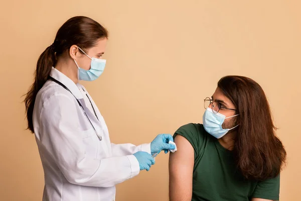 Vriendelijke vrouwelijke arts met gezichtsmasker desinfecterende huid vóór injectie — Stockfoto