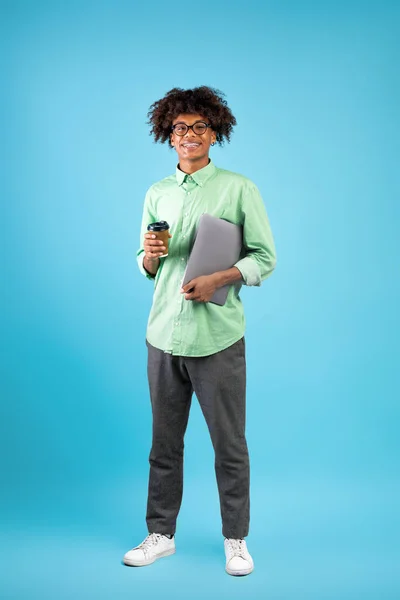 Modern student. Happy black guy with laptop computer and takeaway coffee posing to camera on blue background — Stock Photo, Image