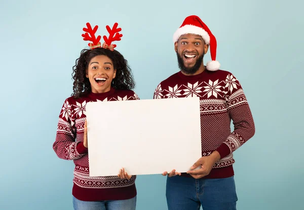 Різдвяна реклама. Щасливий чорний чоловік, який тримає порожній плакат, стоїть над синім тлом, банер — стокове фото