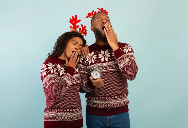 Pareja afroamericana aburrida vistiendo jerséis navideños y cuernos de ciervo, bostezando, cubriendo la boca con las manos — Foto de Stock