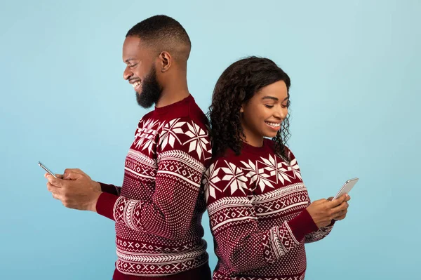 Människor och teknik koncept. Glad svart par som håller smartphones och står tillbaka till ryggen, blå bakgrund — Stockfoto