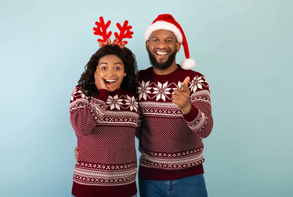 Здивований афроамериканець у різдвяних светрах, що вказують на камеру на синьому фоні. — стокове фото