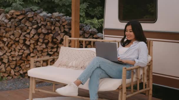 Mujer asiática sonriente usando el ordenador portátil mientras tiene vacaciones en el camping — Vídeos de Stock