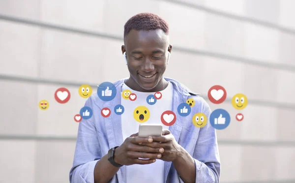 スマートフォン、ソーシャルネットワーク上でオンラインチャットワイヤレスヘッドフォンで魅力的な千年アフロアメリカ人の男を笑顔 — ストック写真