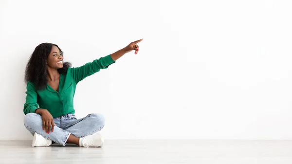 Mujer negra feliz sentada en el suelo, apuntando al espacio de copia —  Fotos de Stock