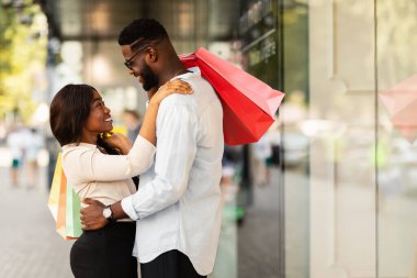 Mutlu afro çift kucaklaşıyor ve alışveriş torbaları tutuyor.