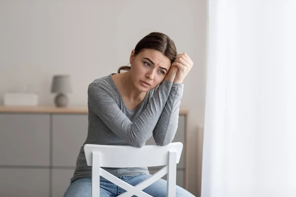 Sconvolta giovane donna si siede da sola, guardando lontano con triste espressione a casa interiore — Foto Stock