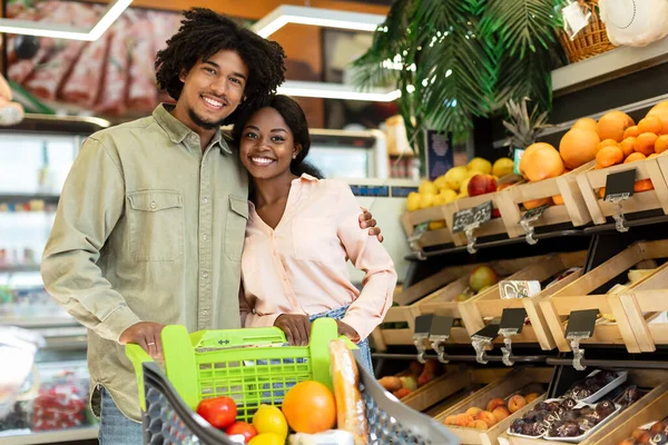 Alegre preto compradores casal posando com carrinho compras no supermercado — Fotografia de Stock