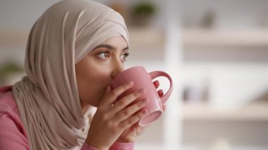 Günaydın. Rahatla. Genç Müslüman kadın tesettürlü sıcak kahve ya da çay içiyor, evinde dinleniyor, fincanı tutuyor ve gülümsüyor.