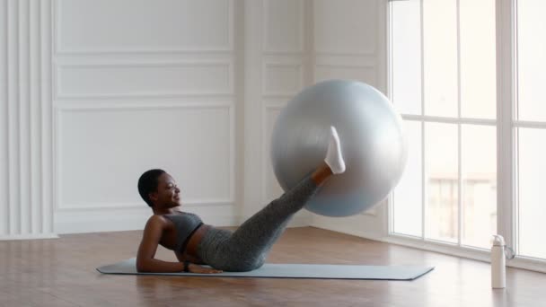 Спортивная молодая черная женщина тренируется с фитболом, поднимая его ногами — стоковое видео