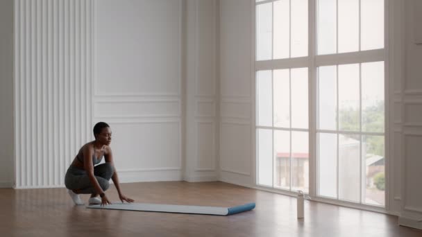 Preparándose para el entrenamiento. Deportiva joven afroamericana mujer desplegando colchoneta de fitness — Vídeos de Stock