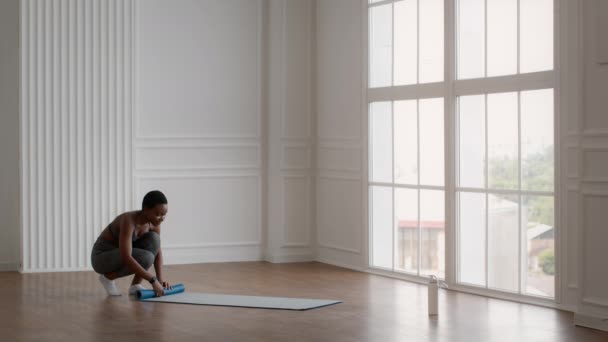 Joven mujer afroamericana deportiva rodando por la alfombra de fitness después de entrenar en casa — Vídeos de Stock