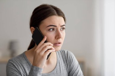 Endişeli üzgün genç bayanın portresi telefonla konuşuyor, evde kötü haberler alıyor.