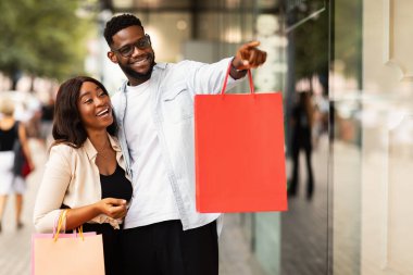 Pencereyi işaret eden alışveriş torbalarıyla neşeli Afrikalı çift