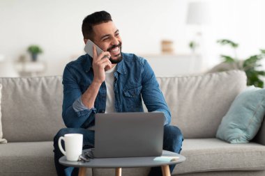 Ev bilgisayarında çalışırken cep telefonuyla konuşan yakışıklı genç bir Arap. Boşluğu kopyala.