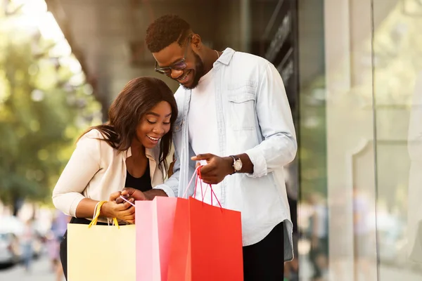 Happy black couple holding shopping bags looking inside — Stock Photo, Image