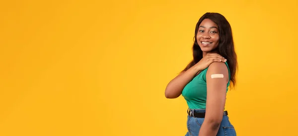 Señora negra vacunada feliz que muestra el brazo con el yeso, fondo amarillo — Foto de Stock