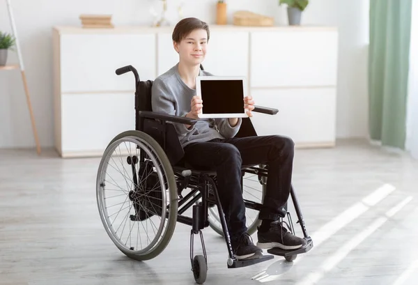 Upośledzony nastolatek na wózku inwalidzkim pokazujący tablet z pustym ekranem w domu, makieta na stronę internetową lub aplikację — Zdjęcie stockowe